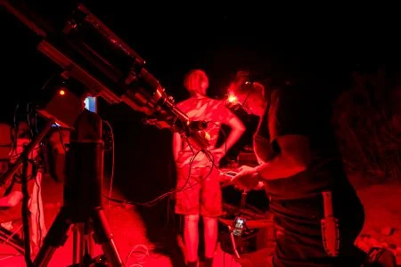 Two people using telescopes under red lights at a nighttime star party