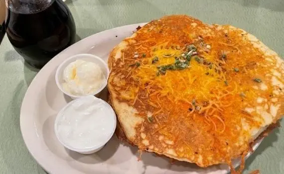 Loaded hash brown pancakes served with sour cream, butter, and syrup on a white plate