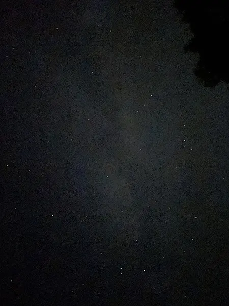 Milky Way band visible in the night sky over Boone, North Carolina, with faint stars and tree silhouette in the corner