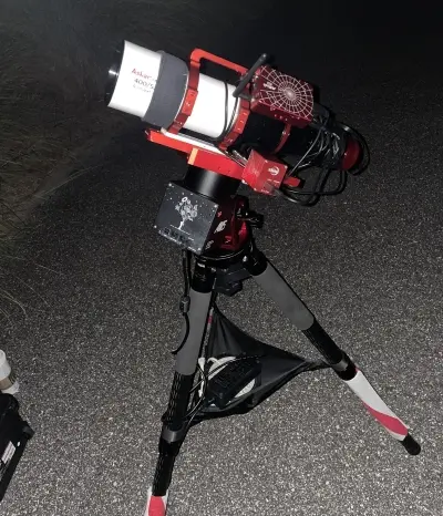 Red and white Askar telescope setup on tripod, captured at night during club star party